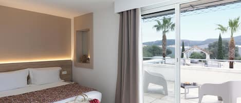 A hotel room with a bed, a bedside table, a large window with a view of palm trees and a distant building, and a balcony with white chairs and a table.