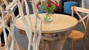 A modern living room with a round wooden table, a vase with red flowers, and a unique wooden sculpture. - Golfe Hôtel (Porto-Vecchio)