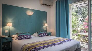 A bedroom with a large bed, two bedside lamps, a nightstand, and a view of a garden through a glass door.