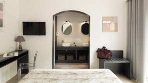 A hotel room with a bed, a desk with a lamp, a TV, a bathroom with a mirror, and a handbag on a bench. - Golfe Hôtel (Porto-Vecchio)