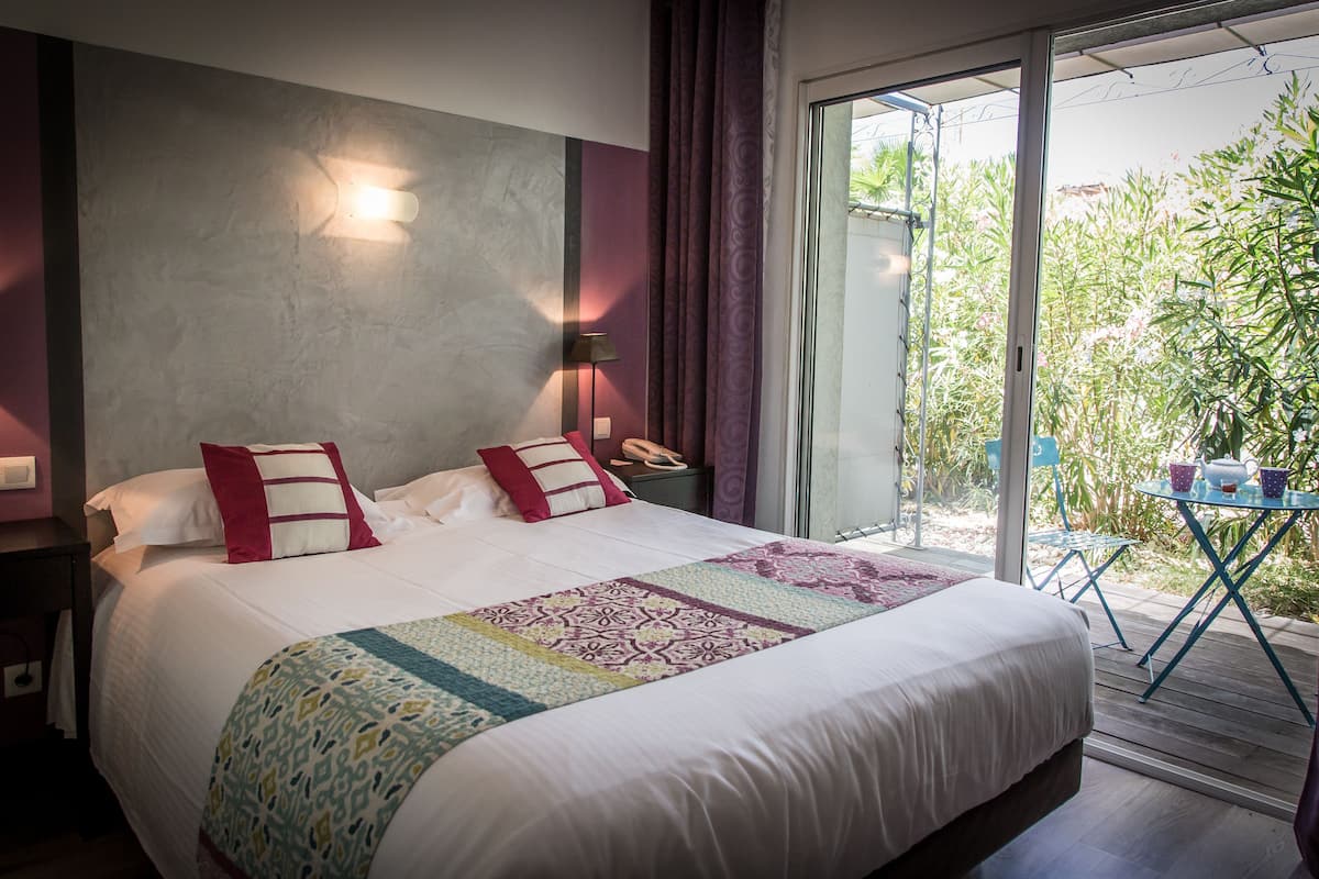 Une chambre d’hôtel avec un grand lit, une table de chevet, une lampe et une vue sur l’extérieur grâce à une porte-fenêtre coulissante.