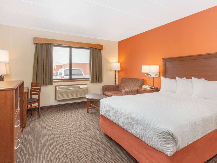 A hotel room with a large bed, a desk with a chair, a small table, and a window with curtains.