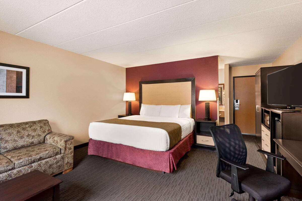 Ein Hotelzimmer mit Bett, Schreibtisch, Stuhl, Fernseher und einer Couch.