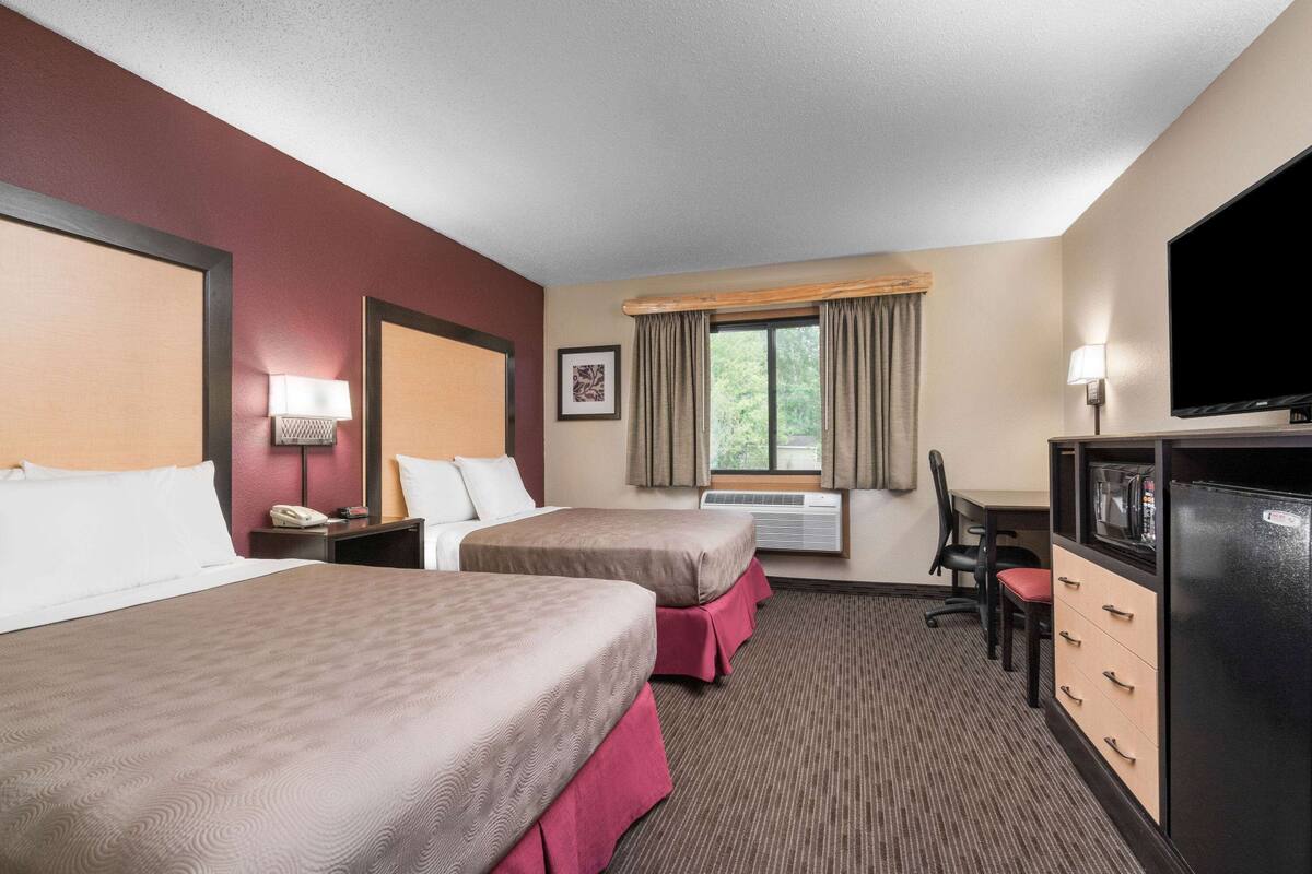 Ein Hotelzimmer mit zwei Betten, einem Schreibtisch, einem Stuhl, einem Fernseher und einem fenster mit Vorhängen.