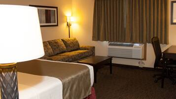 A hotel room with a bed, a desk, a chair, a lamp, a sofa, and an air conditioning unit.