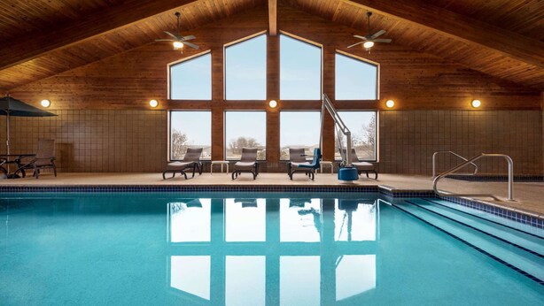 An indoor swimming pool with wooden ceiling and large windows, surrounded by lounge chairs. - AmericInn by Wyndham Detroit Lakes (Detroit Lakes)