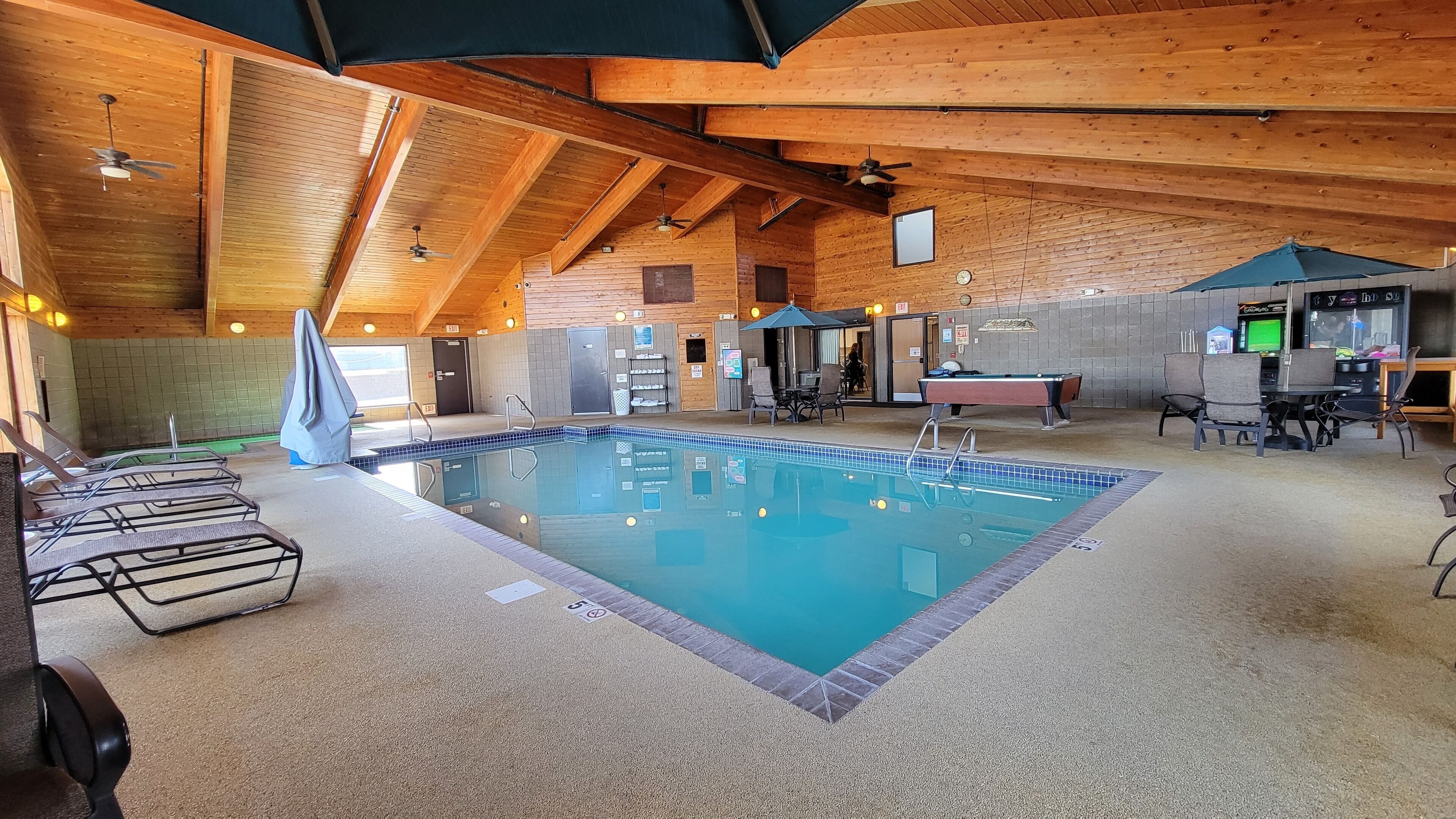 An indoor swimming pool with lounge chairs, a pool table, and a billiards table.