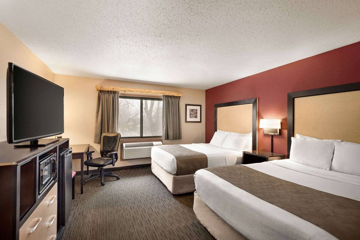Ein Hotelzimmer mit zwei Betten, einem Fernseher, einem Schreibtisch mit Stuhl und einem Fenster mit Vorhängen.
