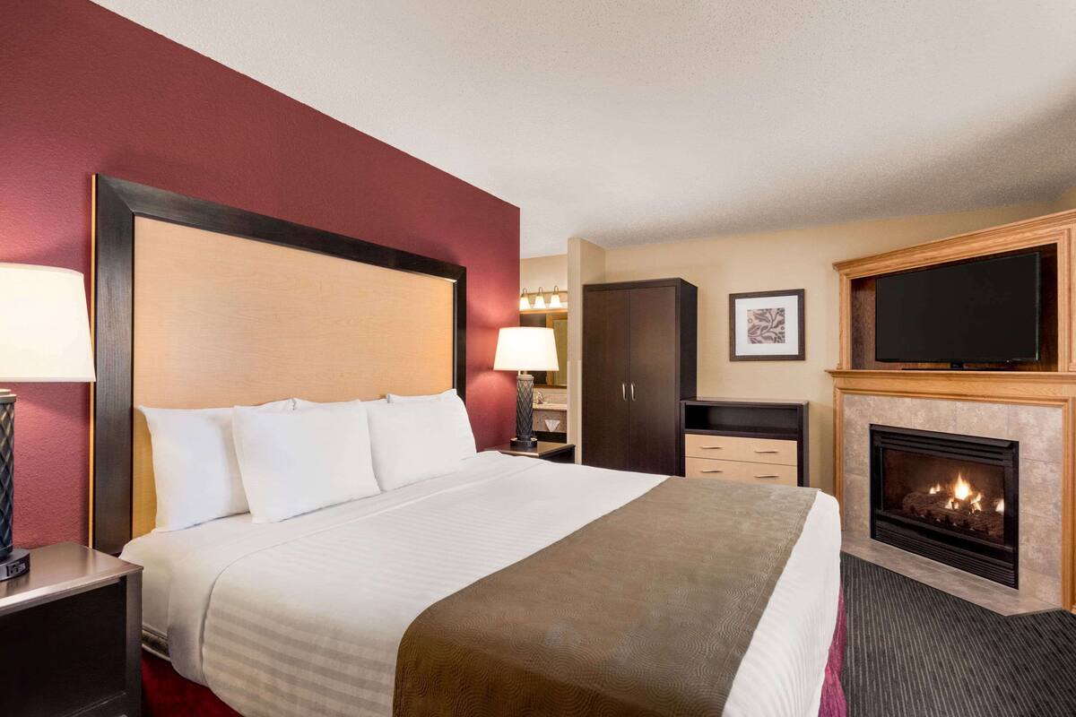 Ein Hotelzimmer mit einem großen Bett, einem Nachttisch mit Lampe, einem Kleiderschrank, einem Fernseher und einem Kamin.