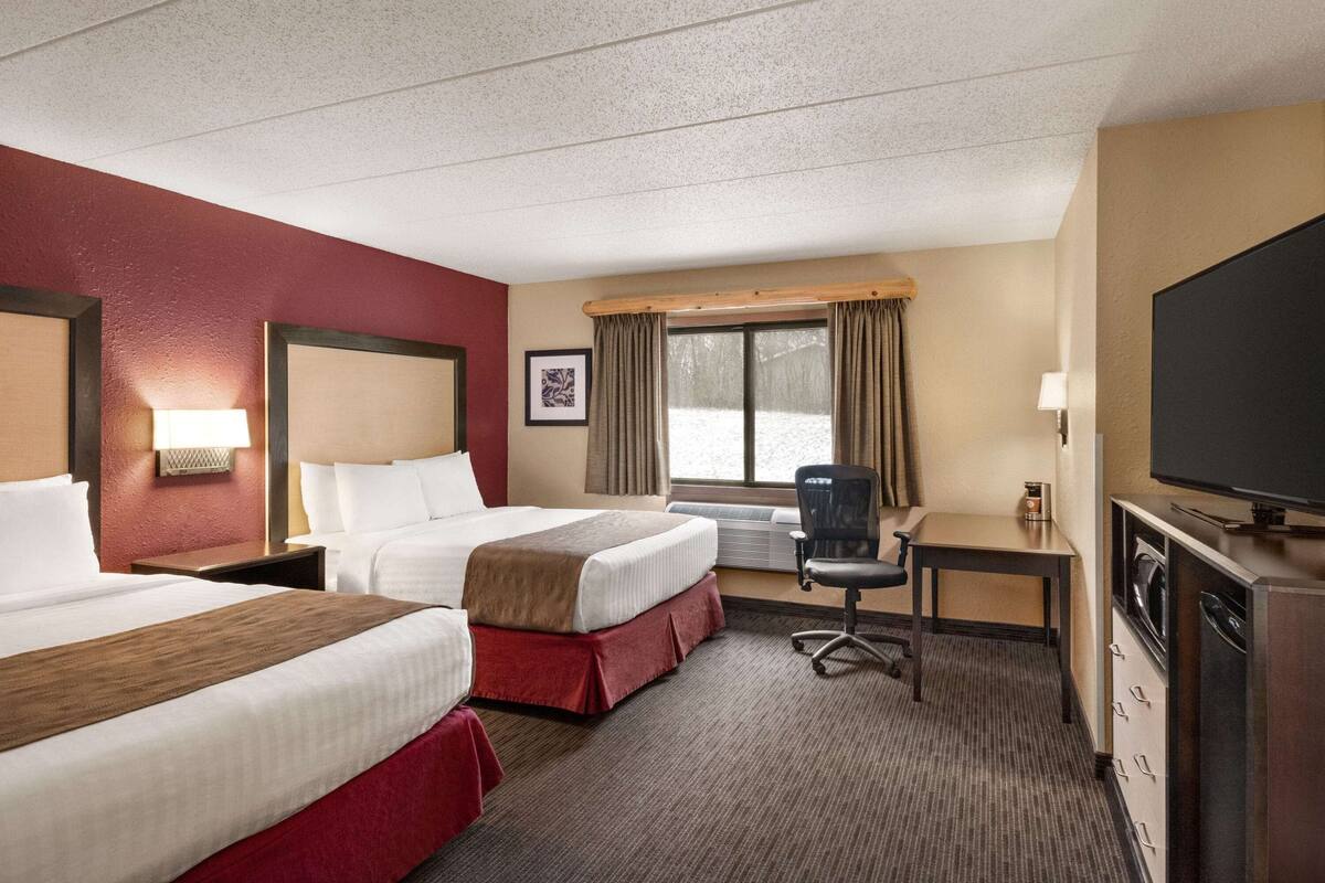 Ein Hotelzimmer mit zwei Betten, einem Schreibtisch, einem Sessel, einem Fernseher und einem Fenster mit Vorhängen.