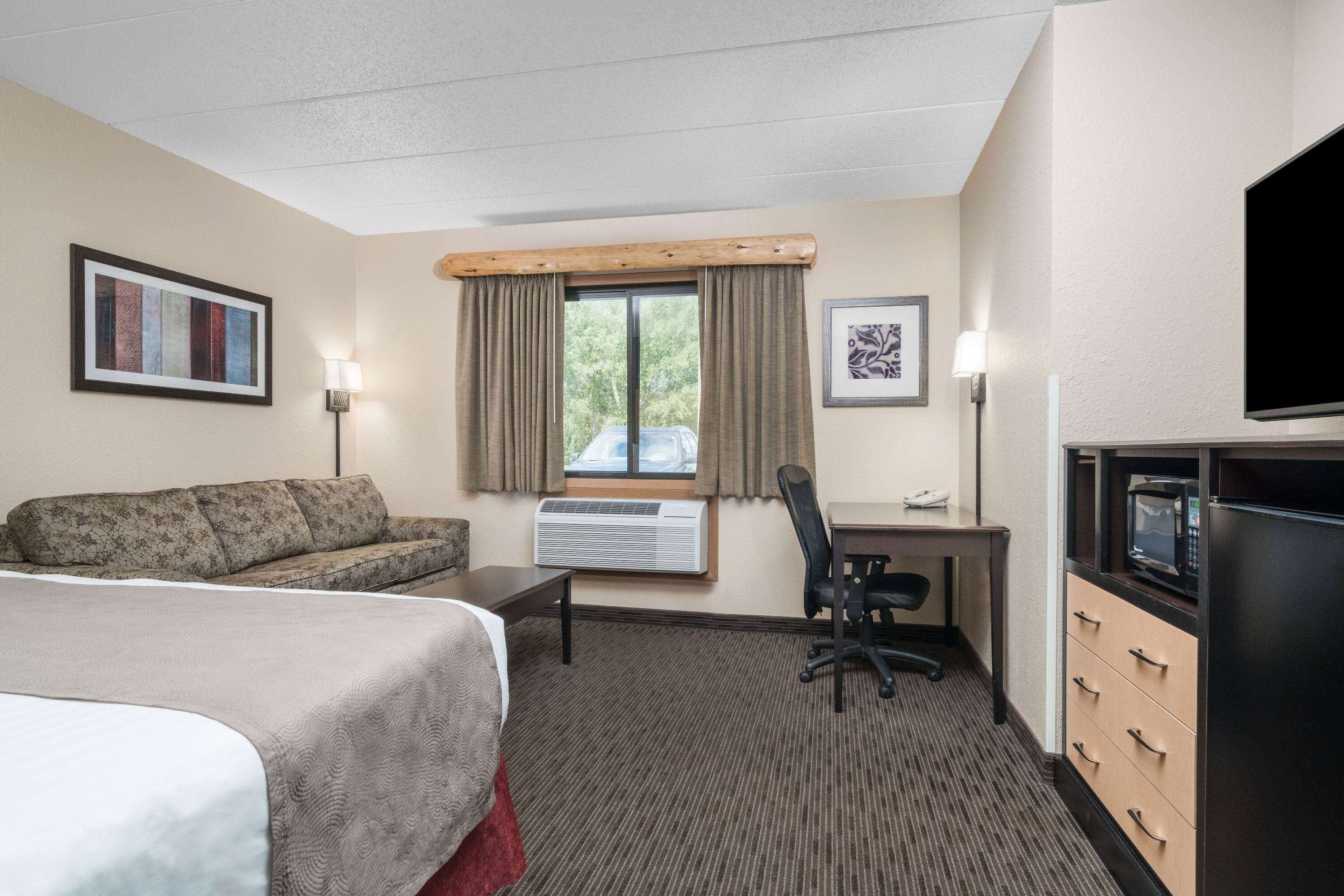 A hotel room with a bed, a desk, a chair, an air conditioning unit, a television, and a microwave.