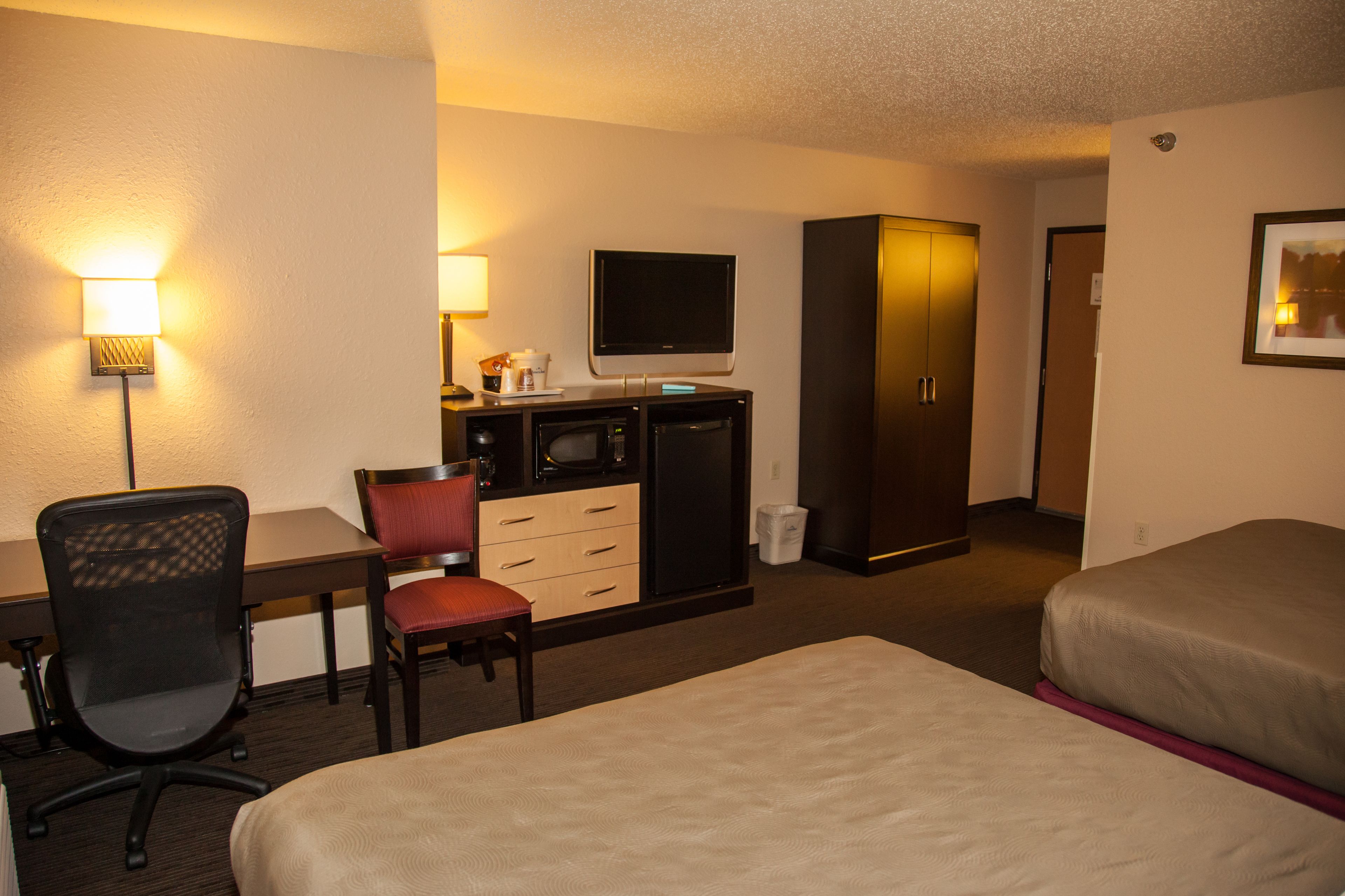 A hotel room with a desk, chair, television, wardrobe, and two beds.