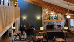 A spacious indoor area with a high ceiling, wooden beams, a stone fireplace, and a TV mounted on the wall. - AmericInn by Wyndham Detroit Lakes (Detroit Lakes)