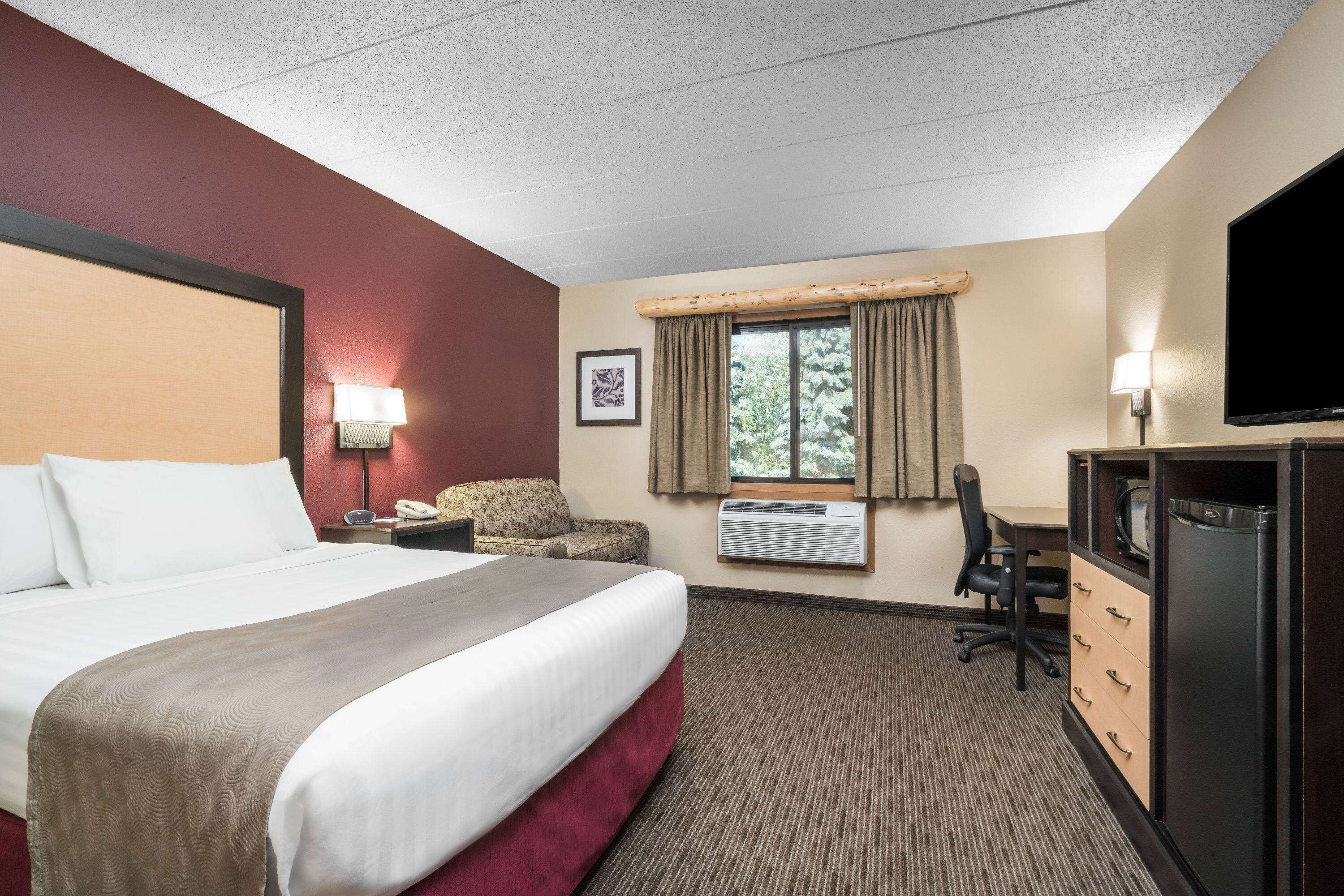 Une chambre d’hôtel avec un grand lit, un bureau avec une chaise, une télévision et une fenêtre avec des rideaux.