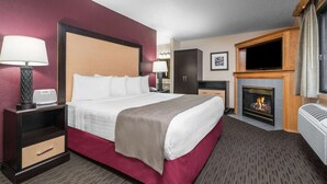 A hotel room with a large bed, bedside lamps, a television, a fireplace, and a desk with a lamp. - AmericInn by Wyndham Detroit Lakes (Detroit Lakes)