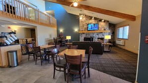 A spacious indoor area with a dining table, chairs, a sofa, and a TV mounted on a stone wall. - AmericInn by Wyndham Detroit Lakes (Detroit Lakes)