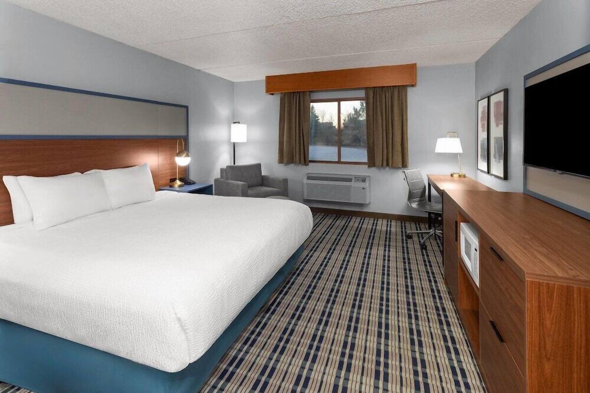 Een hotelkamer met een groot bed, een bureau, een stoel, een televisie en een raam met gordijnen.