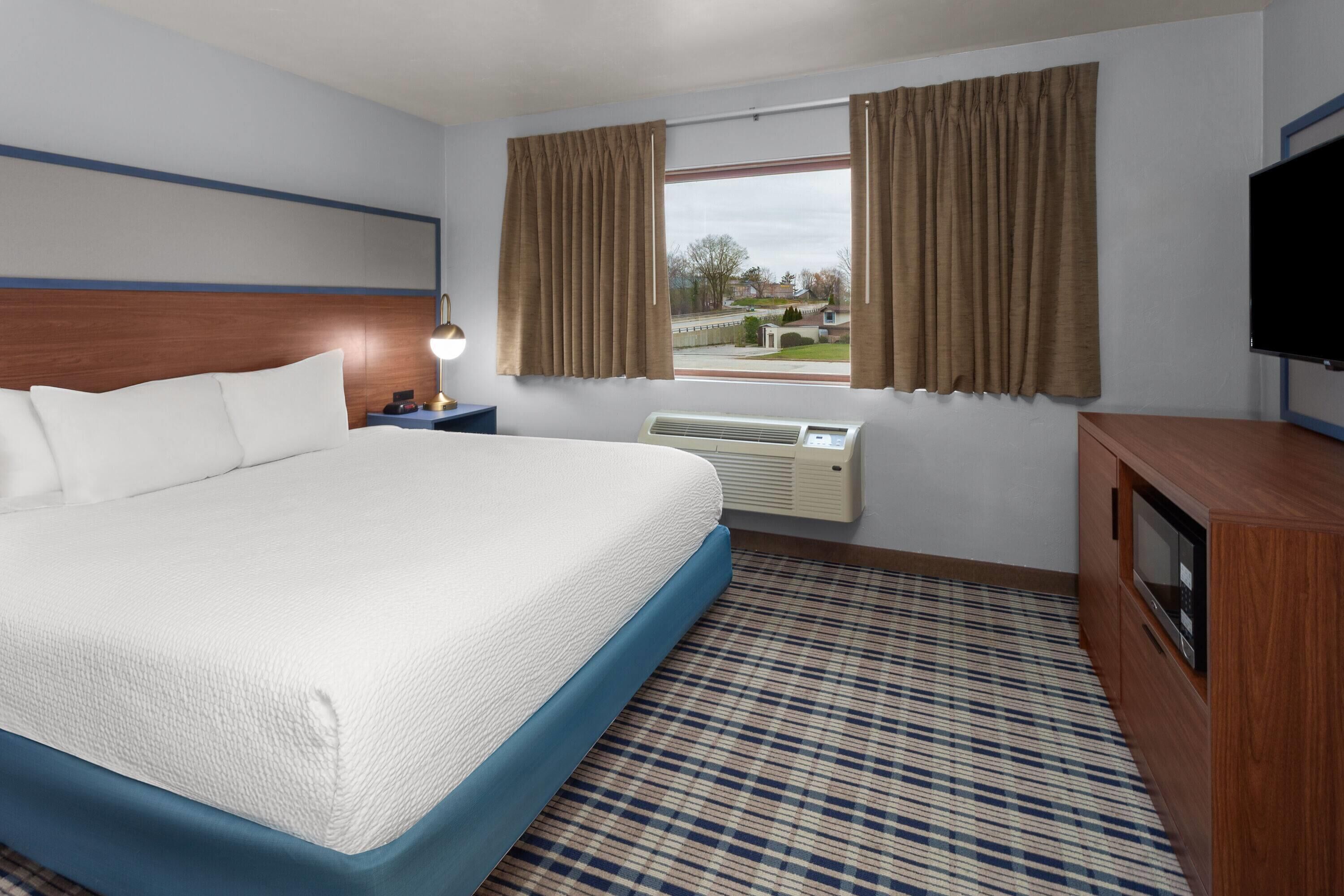 Habitación de hotel con una cama grande, televisión de pantalla plana, escritorio con lámpara y ventana con cortinas.