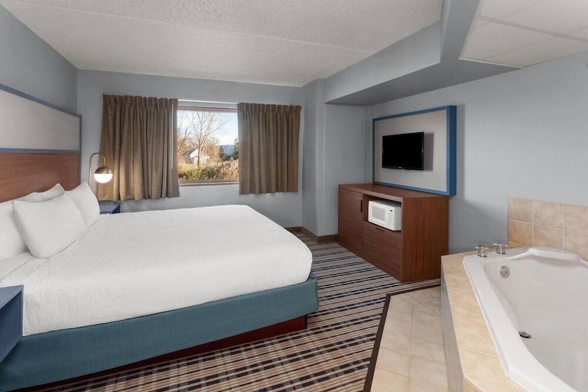 Hotelkamer met een groot bed, een televisie, een badkamer met badkuip en een raam met gordijnen.