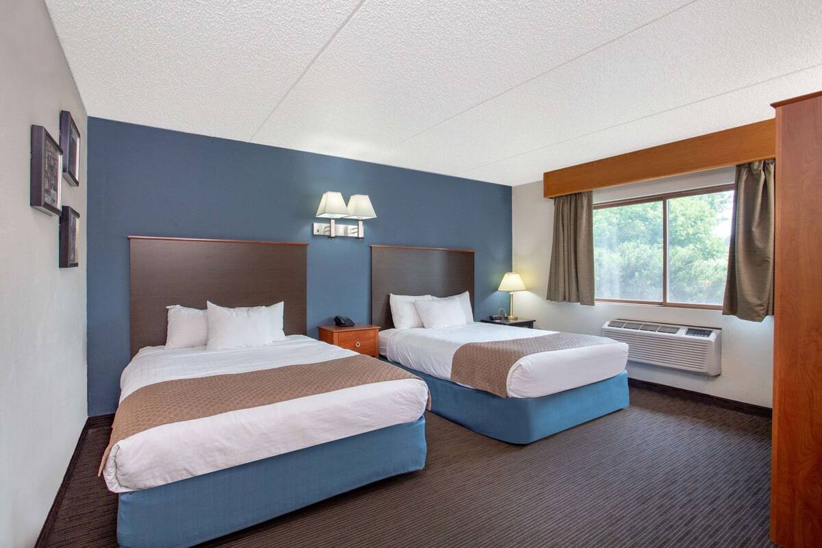 Een hotelkamer met twee bedden, een raam met gordijnen, een wandlamp en een thermostaat.