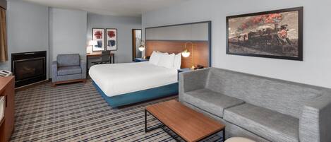 A hotel room with a large bed, a gray sofa, a wooden coffee table, a TV, and a framed picture on the wall.