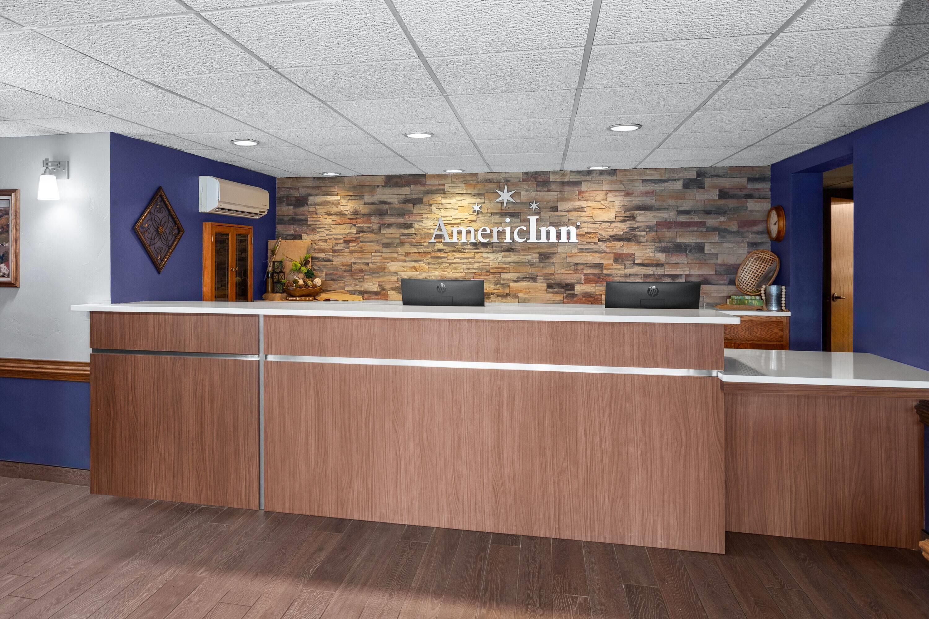 A reception desk with a stone wall backdrop, a sign reading "AmericInn," and a wooden floor.