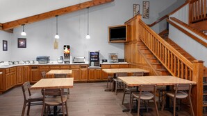 A kitchen with wooden cabinets, a dining area with tables and chairs, a built-in oven, and a staircase. - AmericInn by Wyndham Green Bay West (Green Bay)
