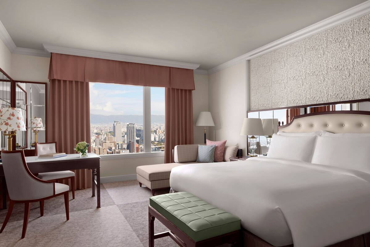 Habitación de hotel con una cama grande, un escritorio con silla, una mesita y vistas a la ciudad.