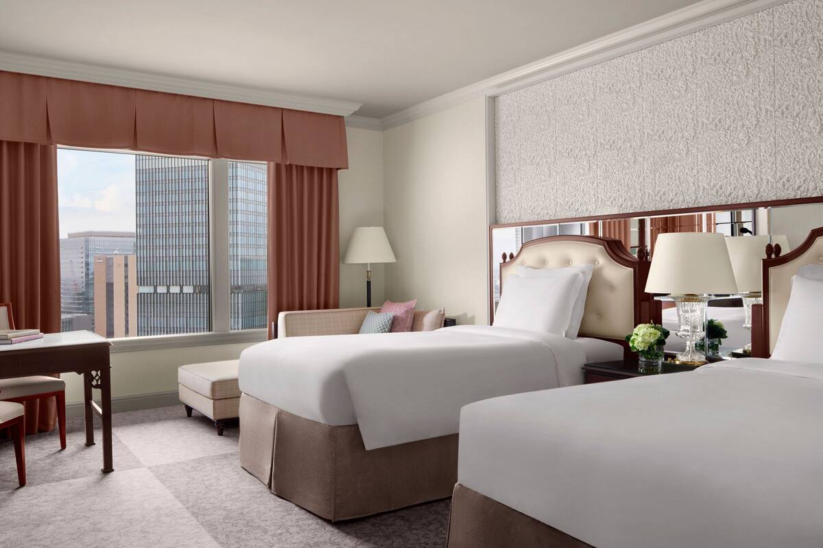 Una habitación de hotel con dos camas, un escritorio, una silla y una ventana con cortinas.