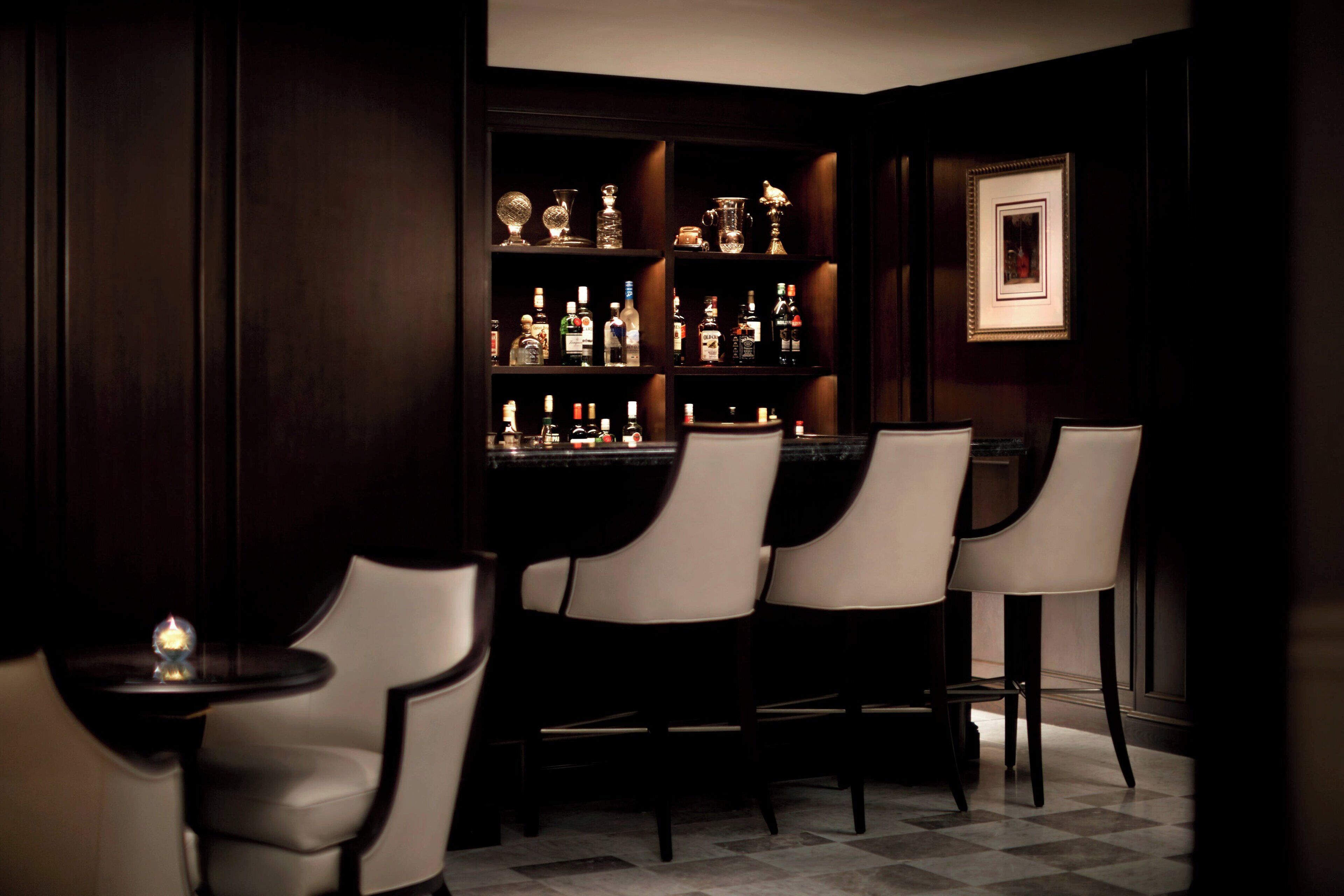 A bar area with a dark wood paneling, a bar counter, and several bar stools.