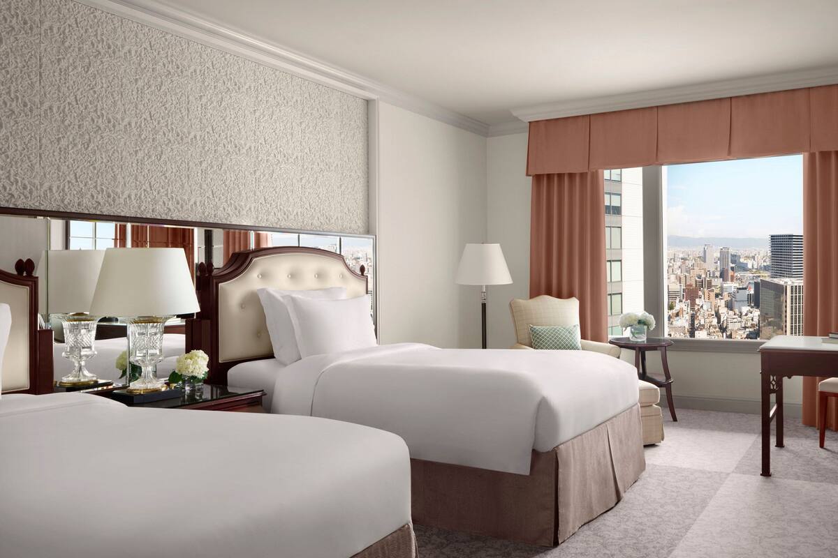 Habitación de hotel con dos camas, un escritorio, una silla y vista a la ciudad.