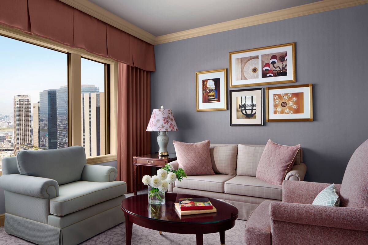 Una sala moderna con vistas a la ciudad, que incluye un sofá, un sillón y una mesa de centro con un jarrón de flores.