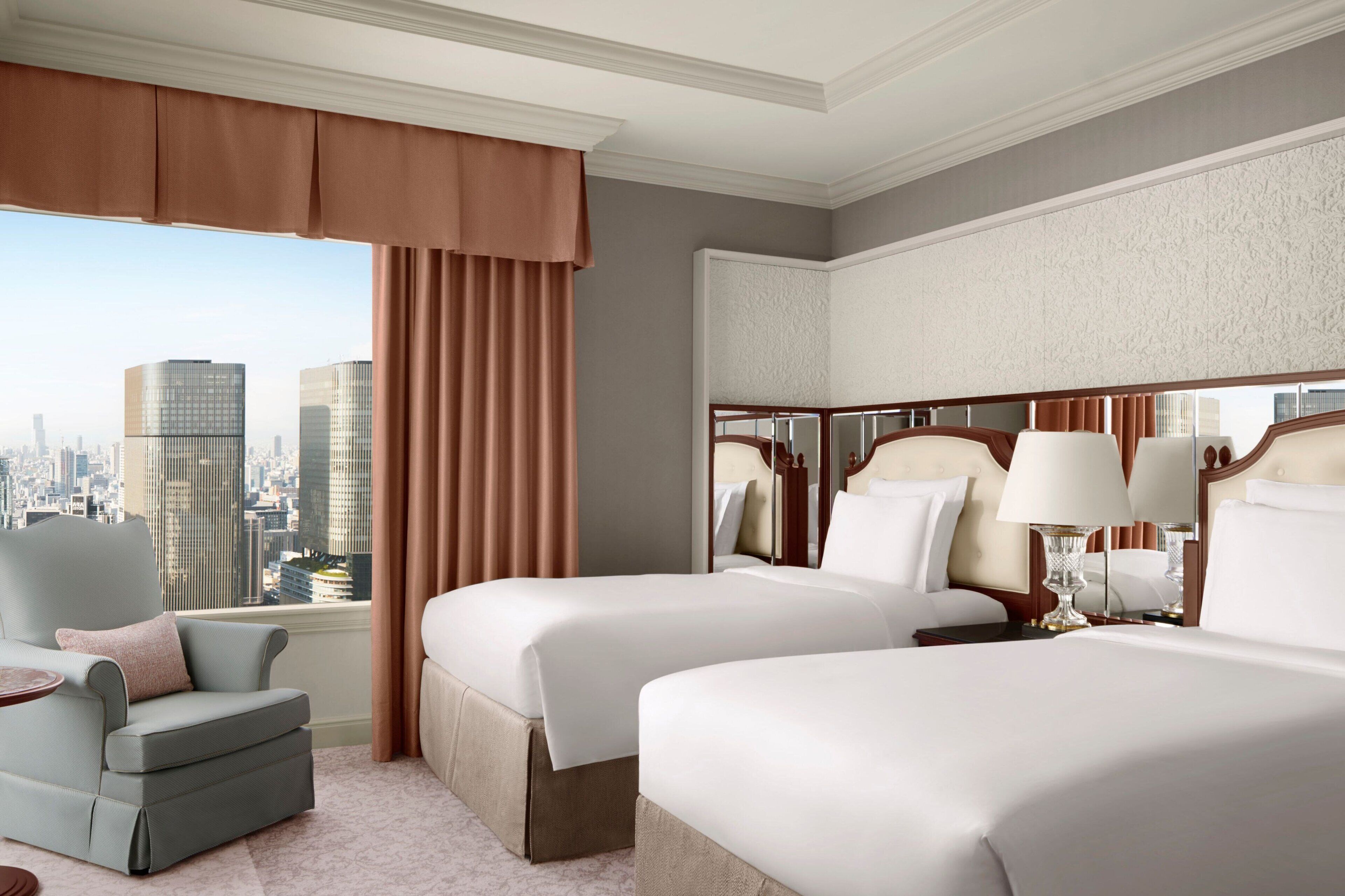 Een hotelkamer met twee bedden, uitzicht op de stad, een raam met stadszicht, een gordijn met stadszicht, een stoel met stadszicht en een tafel met stadszicht.