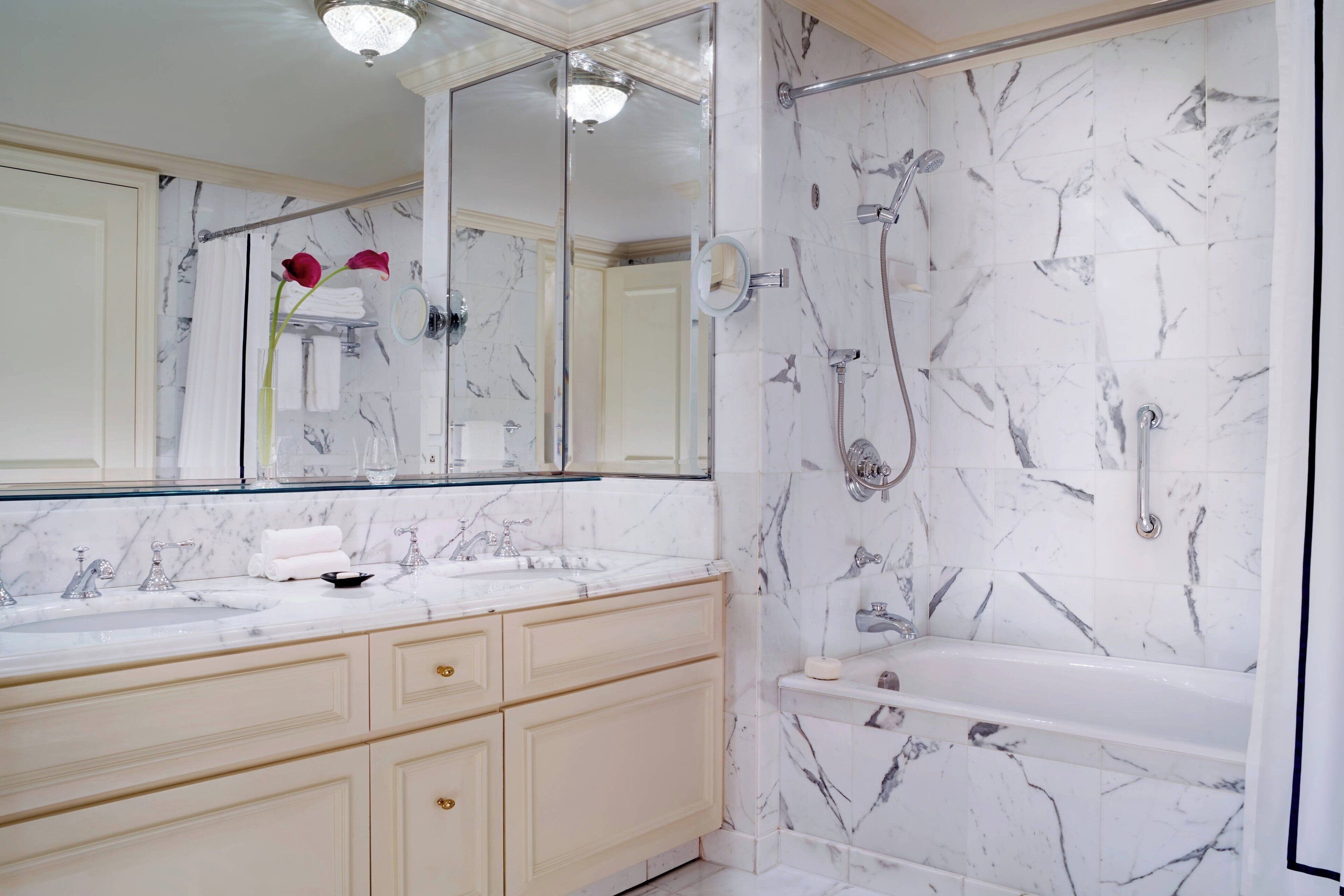 Une salle de bain avec un meuble-lavabo en marbre, un grand miroir, une baignoire et un espace douche.