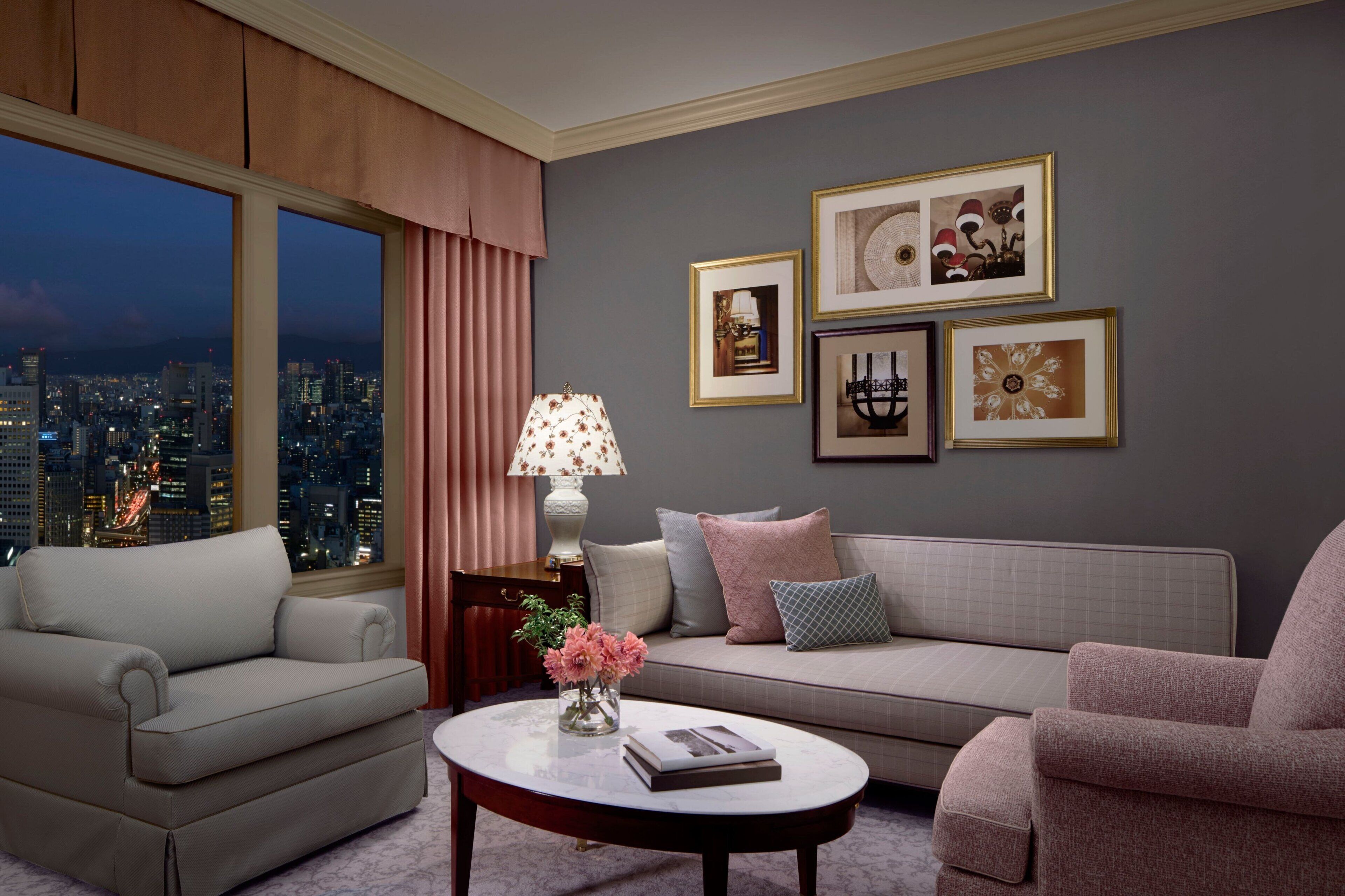 A modern living room with a sofa, armchairs, a coffee table, and a city view through large windows.