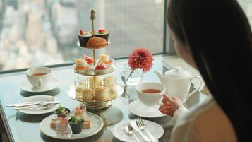 A table set for a tea service with various pastries and desserts, a flower vase, and a city view.