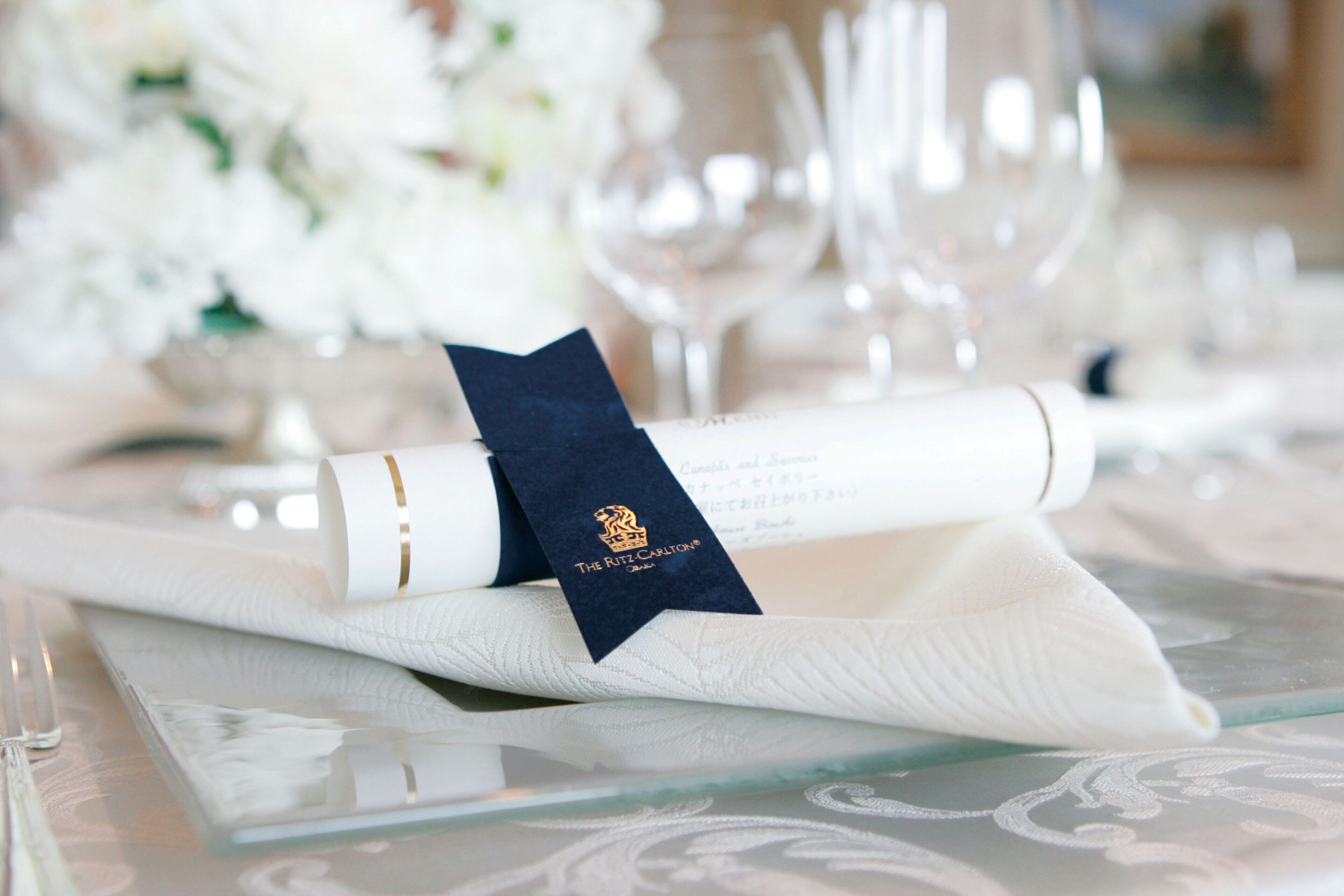 A neatly arranged table with a rolled white napkin, a dark blue napkin with a logo, and a glassware set.