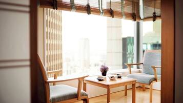 Una habitación con piso de madera, dos sillas de madera, una mesita y una ventana con vistas a edificios.