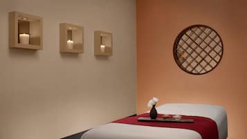 A hotel room with two beds, a red throw blanket, a vase with a flower, and three wall-mounted sconces with candles.