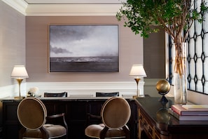 A hotel room with a large framed artwork of a cloudy sea view, a desk with two chairs, and a decorative vase with a globe.
