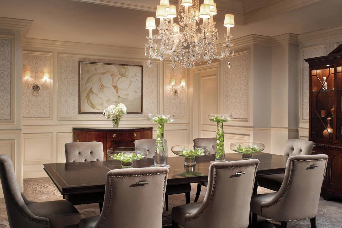 Un comedor elegante con una mesa grande, seis sillas, una araña y apliques de pared.