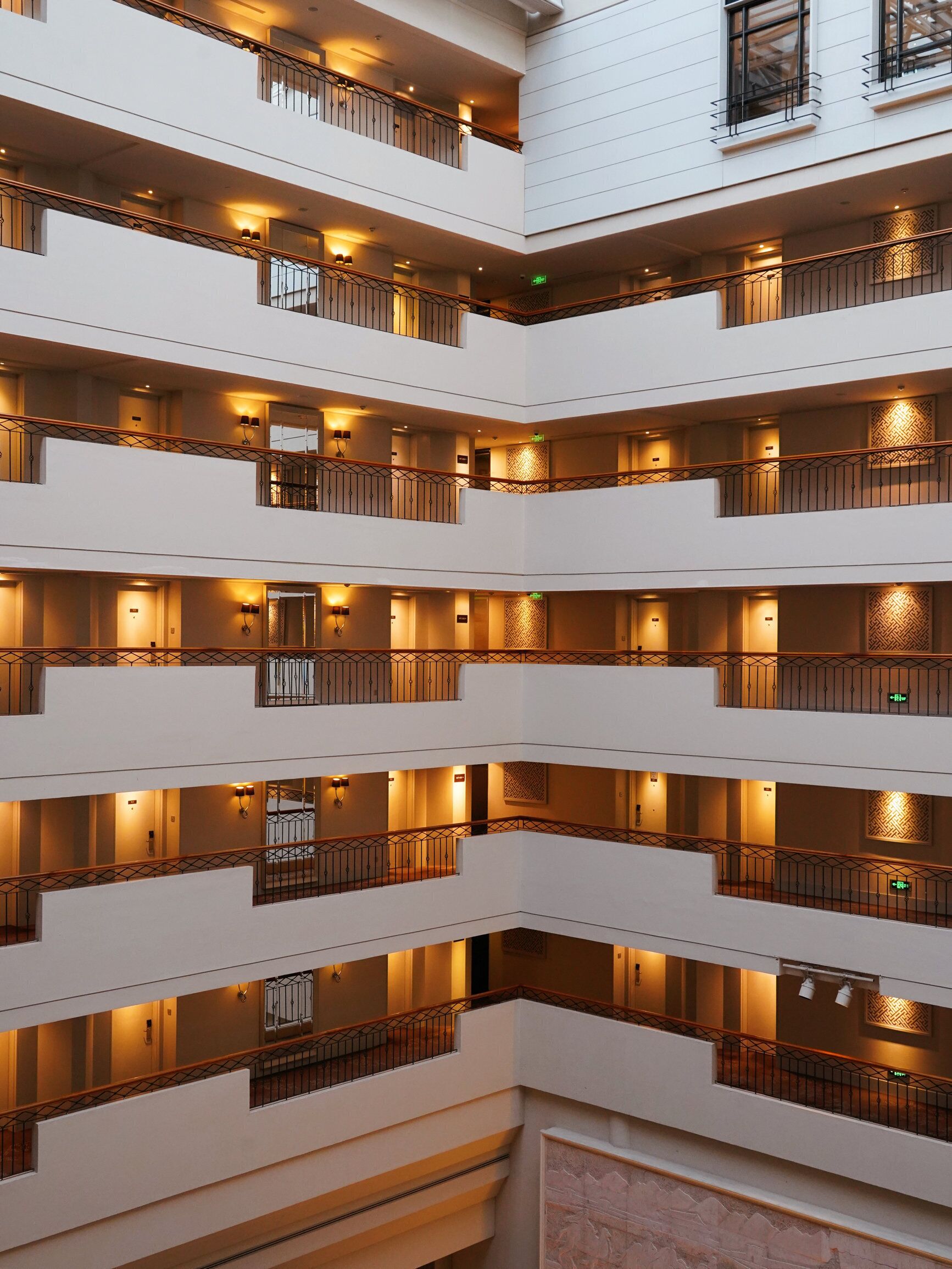 Un intérieur d’hôtel à plusieurs niveaux, doté de balcons, d’escaliers et d’enseignes lumineuses.