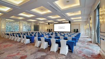 A conference room with rows of tables and chairs, a large screen, and a patterned carpet.
