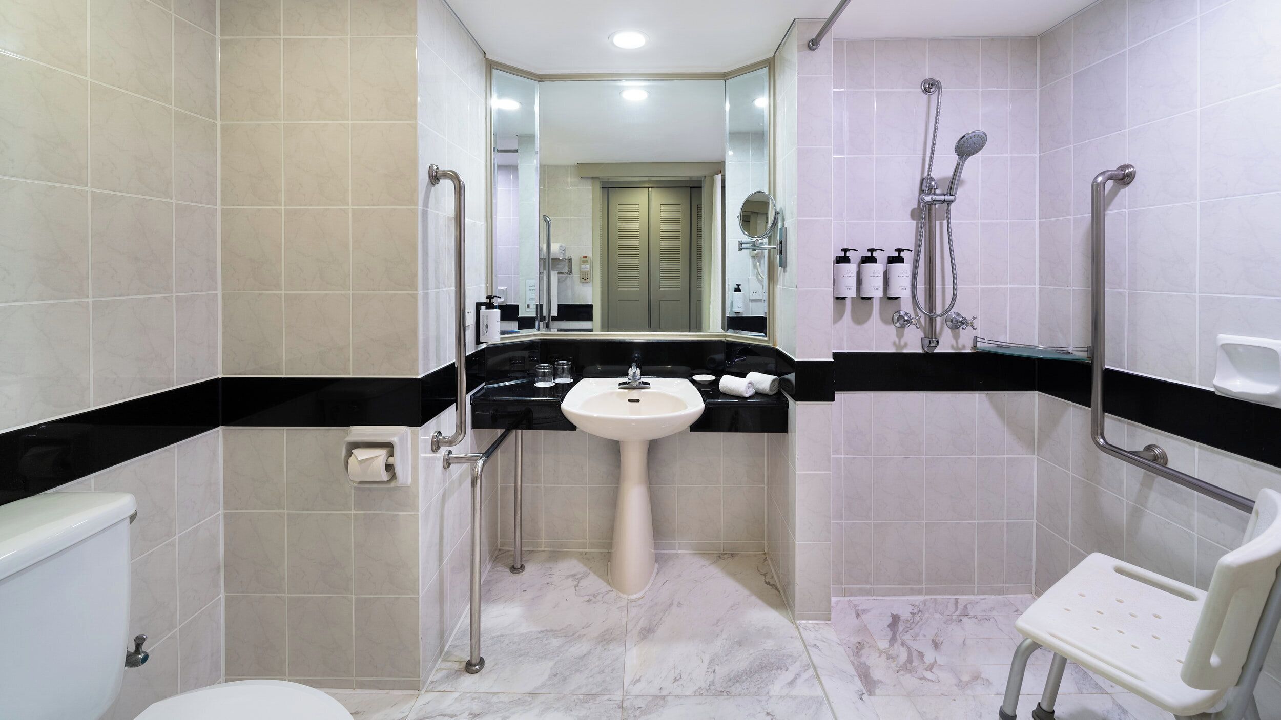 Un baño moderno con lavamanos blanco, encimera negra y cabina de ducha con mampara de cristal.