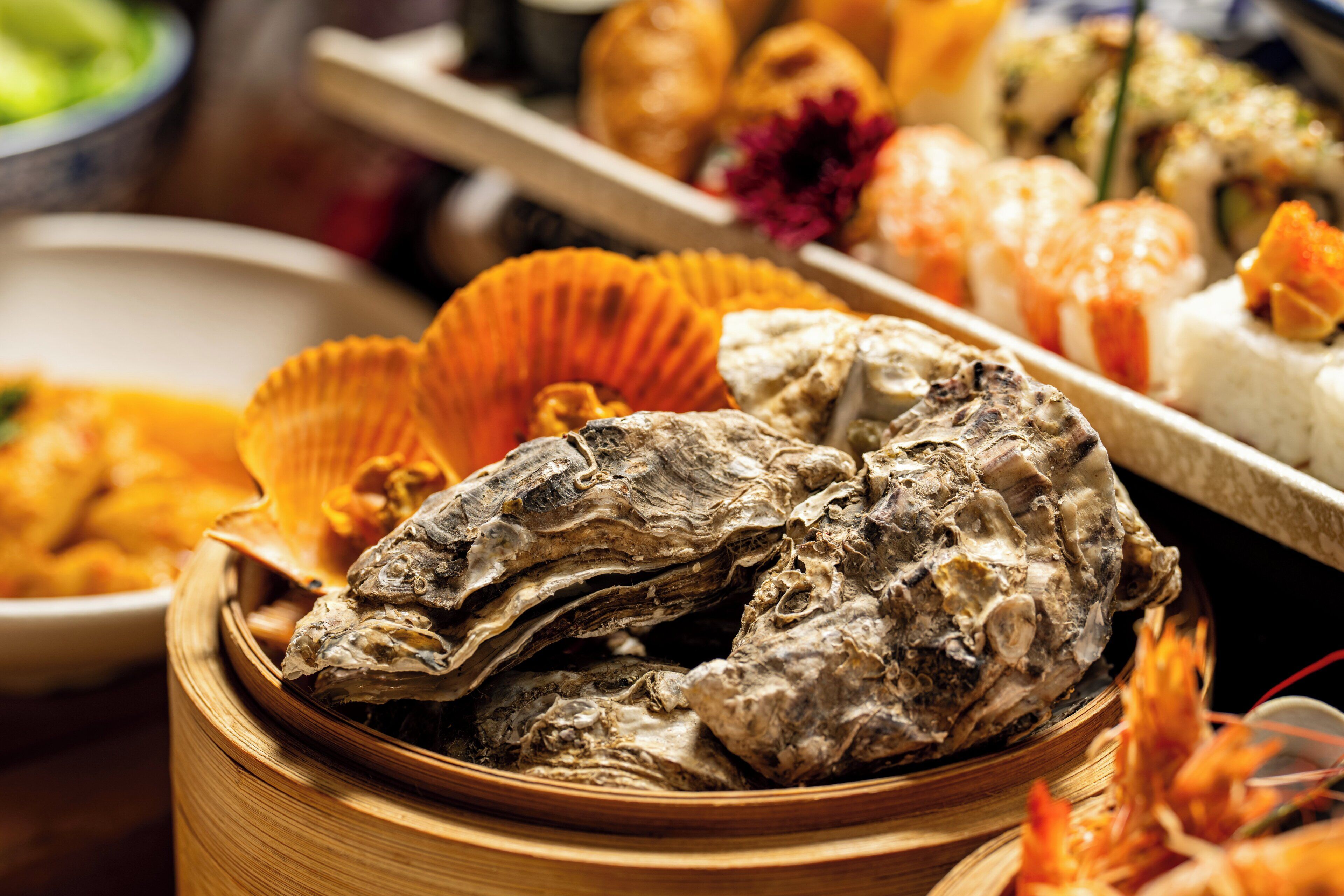 A variety of seafood dishes, including oysters and shrimp, presented in a wooden basket.