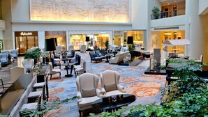 A spacious lobby with multiple seating areas, a piano, and a large mural on the wall.