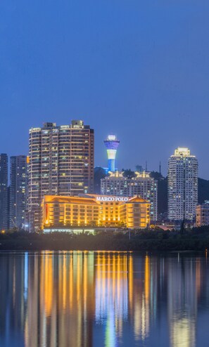 A high-rise building with a prominent tower in the background, reflecting on a body of water. - Marco Polo Xiamen (Xiamen)