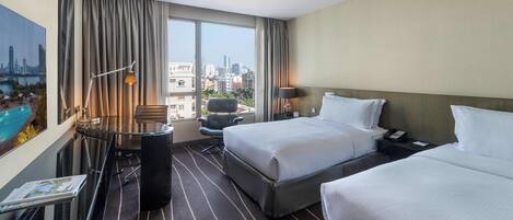 Habitación de hotel con dos camas, un escritorio, una silla, vistas a la ciudad y una piscina.
