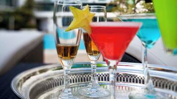 A tray with three glasses of beverages, one with a yellow star, and a green cocktail, set against a hotel backdrop with "MARCO POJ" signage.
