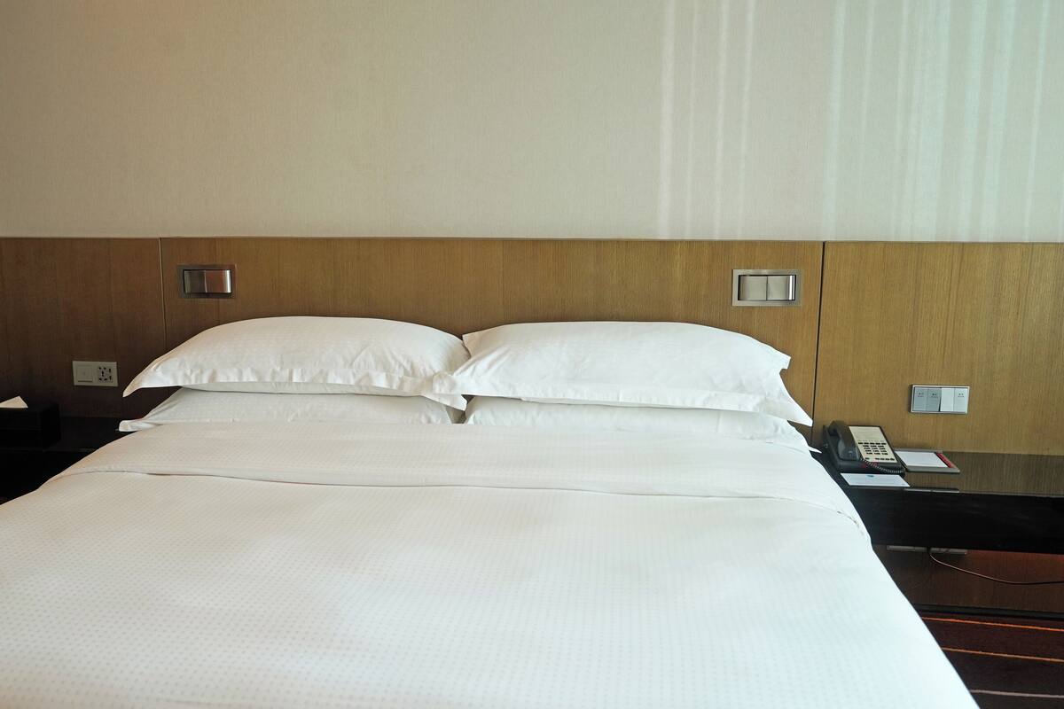 A hotel room with a large bed, two bedside tables, a phone, and a light switch on the wall.